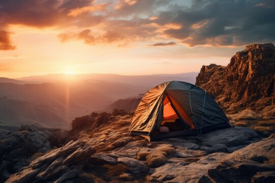 Tent pitched on a rocky cliff overlooking a vast canyon at sunset.