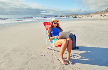 latin american digital nomad woman sitting alone on beach chair doing remote work on her laptop on...