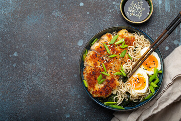 Asian noodles ramen soup with deep fried panko chicken fillet and boiled eggs in ceramic bowl with chop sticks and soy sauce on stone rustic background top view, space for text - 769947576
