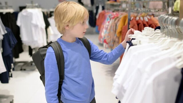 A pretty preteen age boy chooses fashion clothes for himself in a store. Shopping for family with children. An independent child helps his mother in a shopping mall