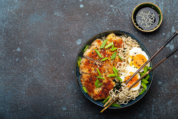 Asian noodles ramen soup with deep fried panko chicken fillet and boiled eggs in ceramic bowl with chop sticks and soy sauce on stone rustic background top view, space for text - 769950176