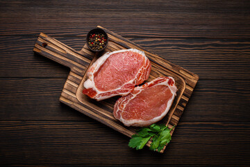 Cut raw meat pork steaks with seasonings on kitchen cutting board, rustic wooden background top view, ready for BBQ. Pork loin chops - 769950721