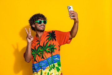 Portrait of friendly guy with afro hair wear shirt in glasses show v-sign make selfie on smartphone...