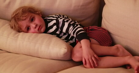 Candid child watching TV screen while laid in living-room sofa