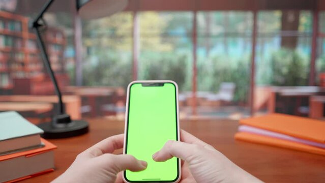 Mobile phone with green screen in hands of woman in background of library. Advertising area, workspace mock up.