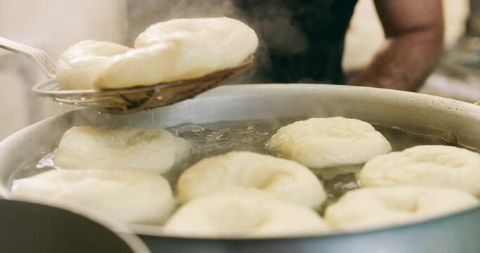 Kitchen, person hands and strainer with bagel in a stove pot with chef, food and bread cooking in restaurant. Cafe, oil and catering of professional baker in bistro working with dough at coffee shop