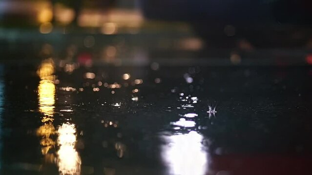 Atmospheric video of rainstorm in a night city. Heavy rain and splashes puddles taken from low point. Large drops break on the pavement in the light of street lamps. Slow motion
