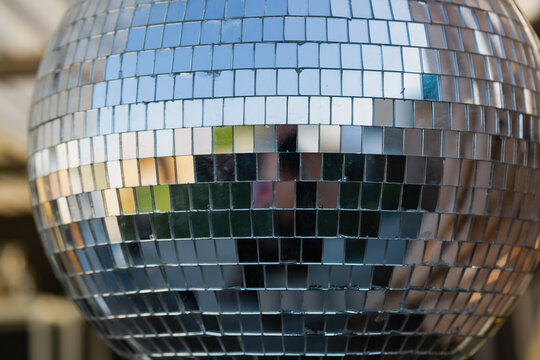 View of a disco ball. It consists of numerous small reflective mirrored tiles. Each tile reflects different colors, shapes from the surrounding environment. The reflections create an abstract pattern