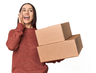 Caucasian young woman with moving boxes on studio background shouting and holding palm near opened mouth.