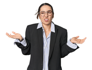 Confident young Caucasian businesswoman on studio background doubting and shrugging shoulders in questioning gesture.