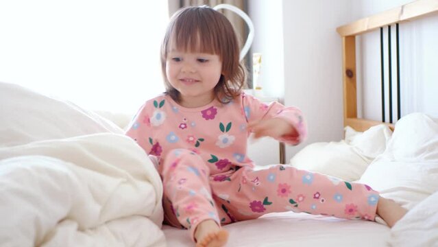 The baby in pajamas woke up and is sitting on the bed. Sunny morning