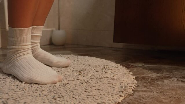 Female legs in white warm socks close-up walking on the toilet mat, the girl takes off her panties before going to the toilet