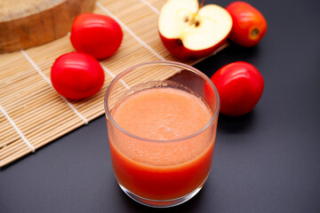 Tomato and apple juice placed on a black background. Fruit juice with apple and tomato with the concept of healthy eating, refreshing, smoothie, and rustic kitchen. Healthy juice of tomato and apple.