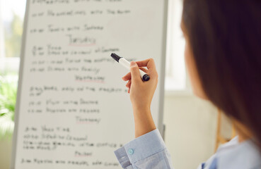 Close up of a young business woman standing in front of business planner holding marker in hand....