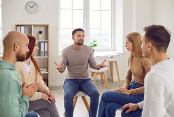 Professional psychotherapist leading group of young adults, helping male and female patients to cure mental health problems through group therapy activities. Group therapy session concept.  - obrazy, fototapety, plakaty
