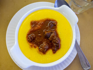 Traditional first course for lunch or dinner in Italy, yellow corn polenta porridge with stew served in Italian restaurant, Milan, Italy