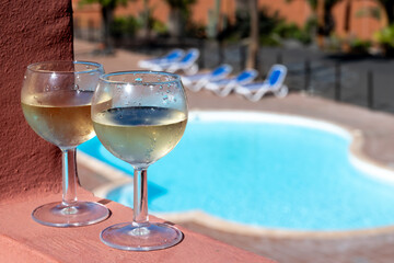 Glasses of cold white wine on roof terrace served outdoor in Corralejo, Fuerteventura in sunny day, pool with blue water