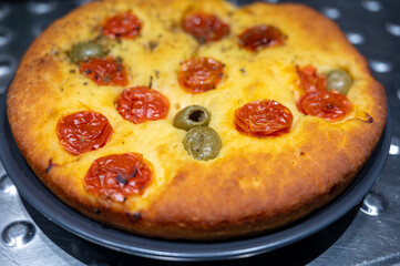 Tasty italian vegetarian food, fresh baked flat foccachia bread with cherry tomatoes, olives and herbs close up