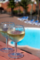Glasses of cold white wine on roof terrace served outdoor in Corralejo, Fuerteventura in sunny day, pool with blue water