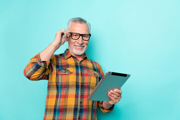 Photo of positive man pensioner dressed checkered shirt glasses holding device empty space isolated teal color background