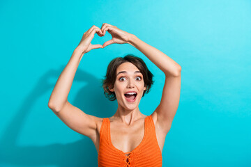 Portrait of impressed ecstatic girl wear orange knit top fingers show heart symbol over head...