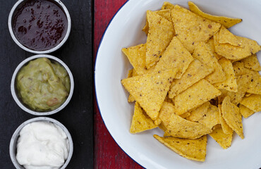 Mexican food. Top view of nachos in a white bowl and three dipping sauces of cheddar cheese, sweet chili and guacamole.	
