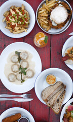 Top view of the restaurant table with drinks and many gourmet dishes such as hamburger, pasta and gourmet french fries
