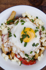 Top view of fried potatoes with melted cheese, chorizo, bell pepper, onion and a grilled egg in a white bowl on the wooden table.	