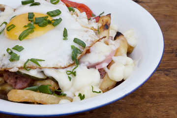 Top view of fried potatoes with melted cheese, chorizo, bell pepper, onion and a grilled egg in a white bowl on the wooden table.