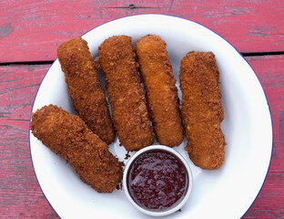 Finger food. Top view of fried breaded mozzarella sticks with dipping barbecue sauce in a white...