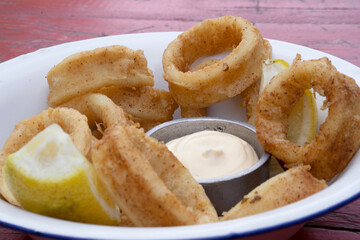Fried seafood. Closeup view of delicious fried squid rings with lemon and a dipping sauce in a...