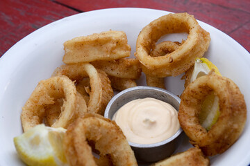 Deep fried seafood. Top view of delicious fried squid rings with lemon and a dipping sauce in a white bowl.	
