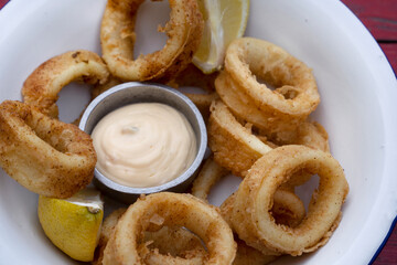 Fried seafood. Top view of delicious fried squid rings with lemon and a dipping sauce in a white bowl.	