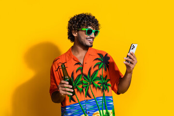 Photo of positive man with afro hairdo dressed print shirt in sunglass hold beer look at smartphone...