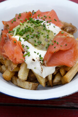 Closeup view of french fries with smoked salmon, cream cheese and guacamole sauce in a white bowl on the wooden table.