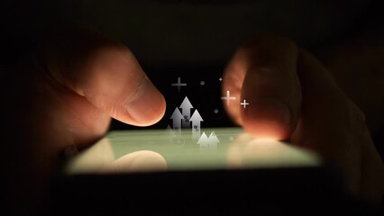 Hands use a smartphone in the dark against the background of which arrows with percentages move and plus signs appear. Cg footage