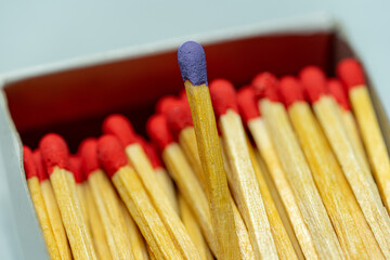 Set of several defocused red-headed matchsticks with one blue-headed matchstick in evidence.