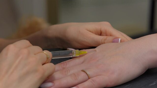 The cosmetologist makes an injection of a medicine for skin rejuvenation on a woman's hand.