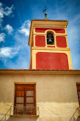 Maroon bell tower of the Parroquia de San Bartolome in Librilla, Murcia, Spain protruding from...