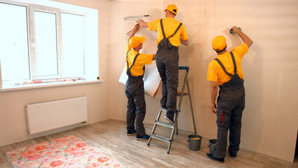 Specialists wallpapering in the house. Brigade of craftsmen making renovation.
