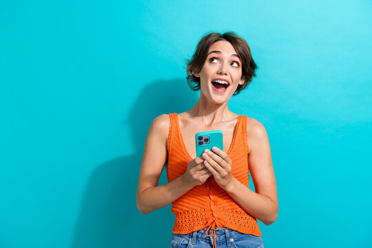 Portrait of overjoyed girl with short hair wear orange knit top look at sale empty space hold smartphone isolated on blue color background