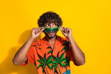 Portrait of ecstatic guy with afro hair wear hawaii shirt touch glasses look at promo empty space isolated on yellow color background