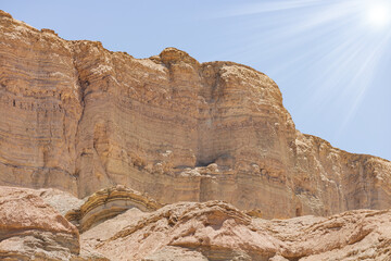 Large rocky mountain with intricate textures and patterns. It is characterized by multiple layers of rock that have been eroded over time. The sky above the rocky formation is clear and blue. Israel.