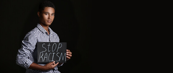 Sad African-American teenage boy with poster on dark background. Stop racism