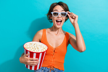 Portrait of ecstatic positive girl wear orange knit top touch 3d glasses hold popcorn staring at...