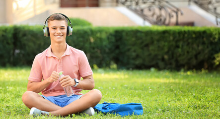 Teenage boy listening to music in park - obrazy, fototapety, plakaty