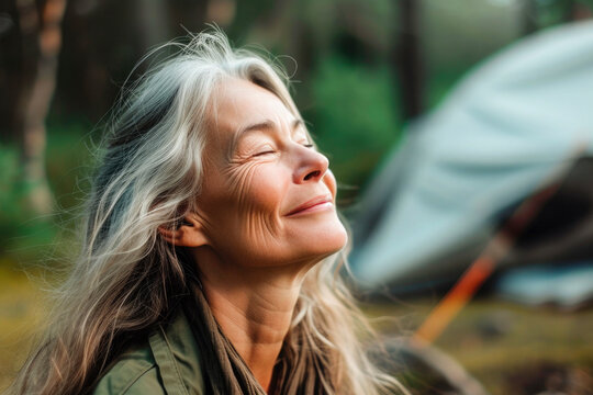 woman with eyes closed breathing fresh air while camping in woods.