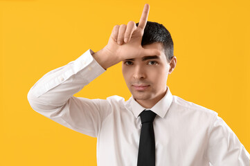 Young businessman showing loser gesture on yellow background, closeup