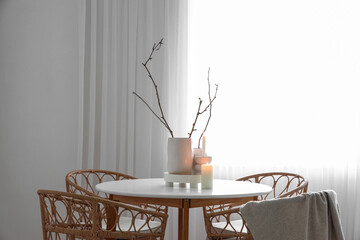 Stylish table with burning candles and rattan chairs in interior of light living room