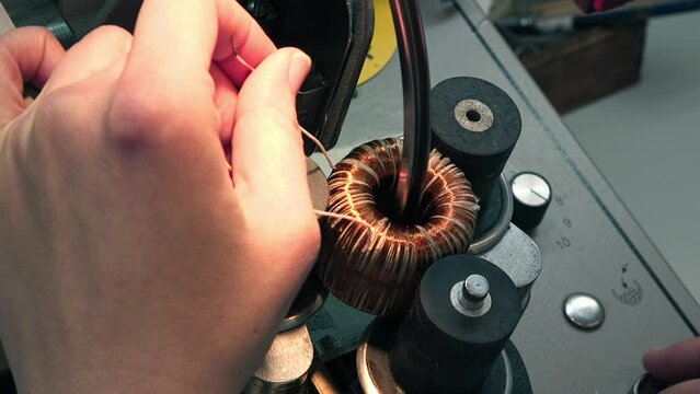 An engineer adding the copper wires into the coil machine. An engineer coiling multiple copper wires using a factory machine. Engineer winding the wires with an industrial coil machine.